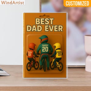 May include: A framed artwork with the text "BEST DAD EVER" and a graphic of a father and two children on bicycles. The father wears a green helmet and jersey with the number 20. The children wear orange and yellow helmets. The word "CUSTOMIZED" is at the top.