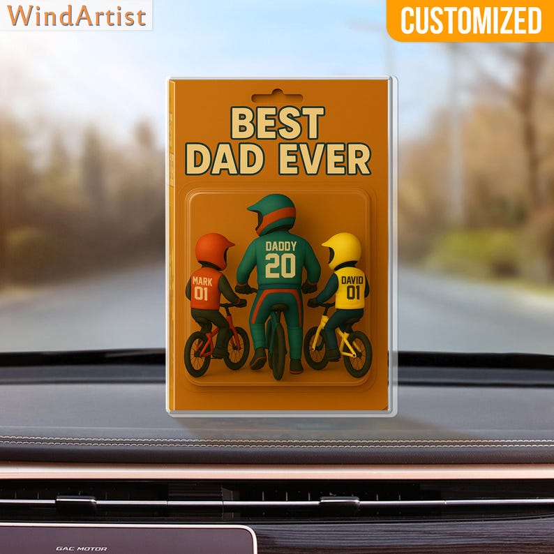 May include: A customized car ornament featuring a father and two children on bicycles. The text "BEST DAD EVER" is displayed above the figures. The father wears a green helmet and jersey with the number 20. The children wear orange and yellow helmets.