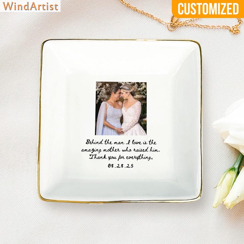 May include: A square, white ceramic trinket dish with a gold rim. The dish features a photo of two women in wedding dresses. Text on the dish reads: "Behind the man I love is the amazing mother who raised him. Thank you for everything, 08.28.25."