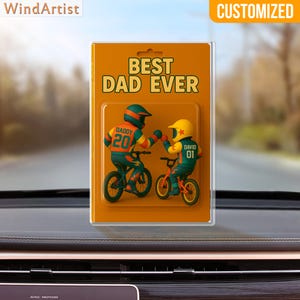 May include: A customized car air freshener with the text "BEST DAD EVER." The design features two cartoon figures on bicycles, one with "DADDY 20" and the other with "DAVID 01." The background is a blurred outdoor scene.