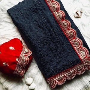 Pu&ograve; includere: Un sari grigio scuro con un bordo ricamato rosso e oro. Il sari ha un bordo a festoni ed &egrave; decorato con piccole paillettes. Il sari &egrave; abbinato a una blusa rossa con un bordo ricamato abbinato.