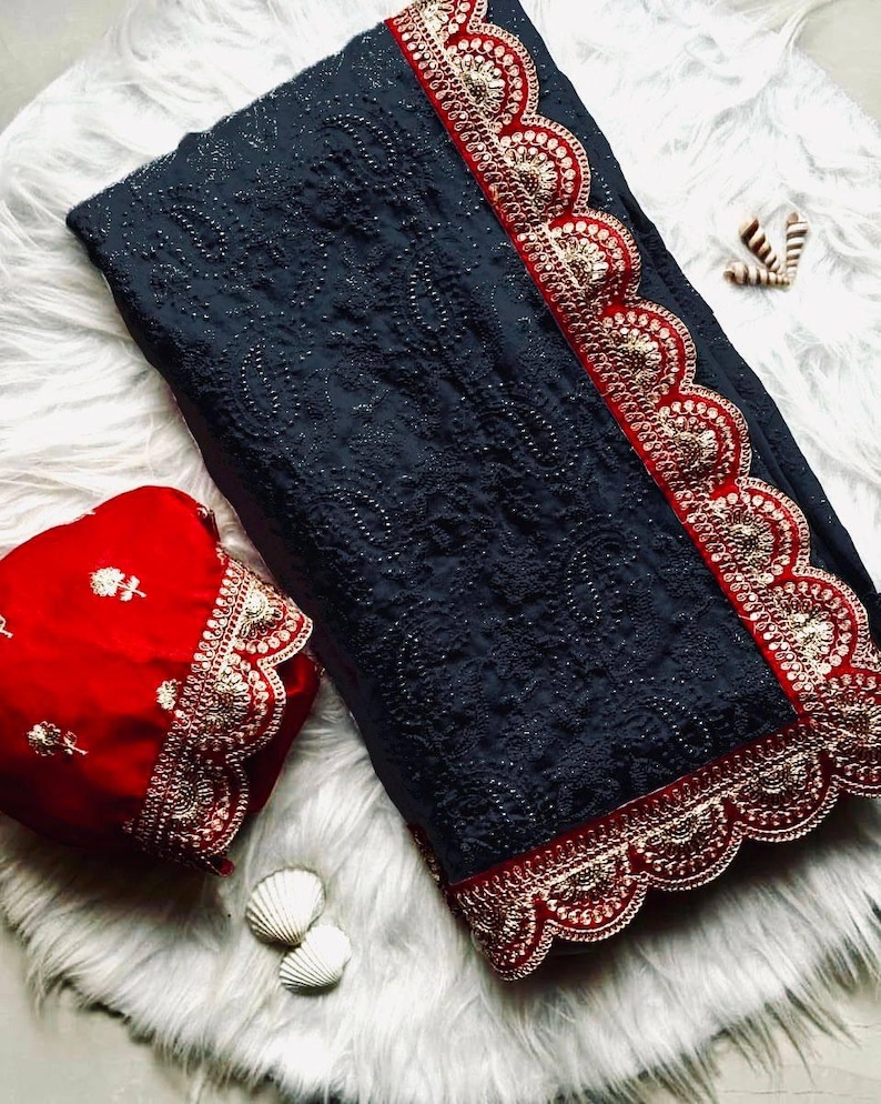 Pu&ograve; includere: Un sari grigio scuro con un bordo ricamato rosso e oro. Il sari ha un bordo a festoni ed &egrave; decorato con piccole paillettes. Il sari &egrave; abbinato a una blusa rossa con un bordo ricamato abbinato.