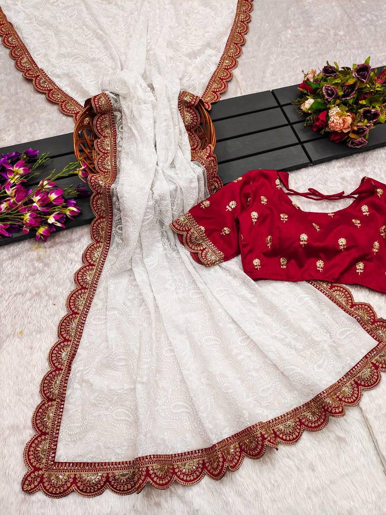Pu&ograve; includere: Sari bianco in rete con bordo ricamato rosso e oro. Il sari ha un bordo a festoni ed &egrave; abbinato a una blusa ricamata rossa.