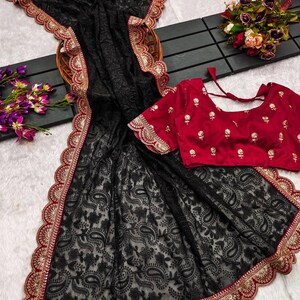 Pu&ograve; includere: Sari nero in rete con un bordo ricamato rosso e oro. Il sari presenta un motivo paisley ed &egrave; abbinato a una blusa ricamata rossa.