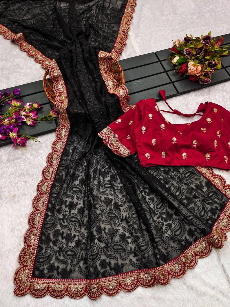 Pu&ograve; includere: Sari nero in rete con un bordo ricamato rosso e oro. Il sari presenta un motivo paisley ed &egrave; abbinato a una blusa ricamata rossa.