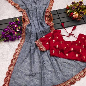 Pu&ograve; includere: Un sari di rete grigio con un bordo ricamato in rosso e oro. Il sari ha un bordo a festoni ed &egrave; abbinato a una blusa rossa con ricami dorati.