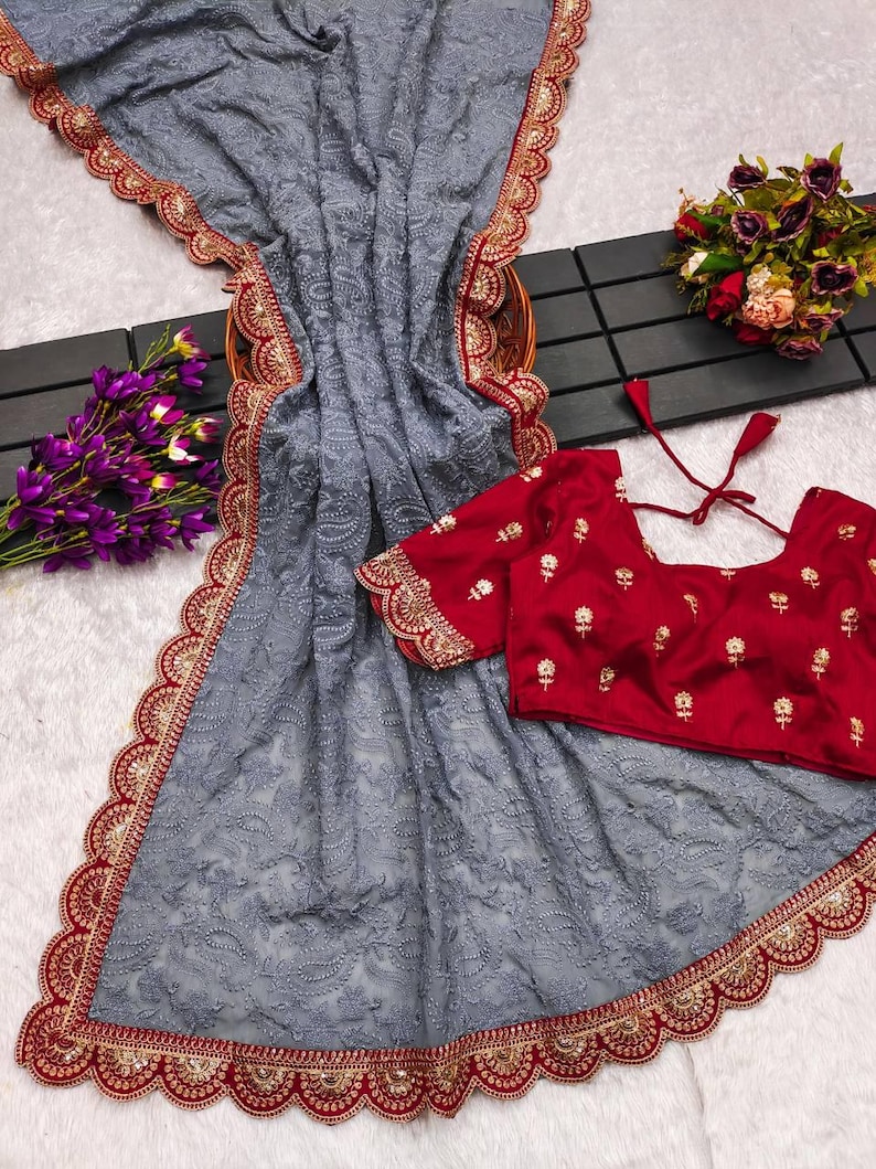 Pu&ograve; includere: Un sari di rete grigio con un bordo ricamato in rosso e oro. Il sari ha un bordo a festoni ed &egrave; abbinato a una blusa rossa con ricami dorati.