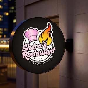 May include: A round, black restaurant sign with the text "Shera's Restaurant" in pink script, a chef's hat, and a flame graphic. The sign also includes the words "TRUE FLAVORS CUISINE" in white. The sign is mounted on a gray brick wall.