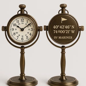 May include: Two antique-style brass clocks. One clock face shows the time, the other displays coordinates and the text "SV MARINER". Each clock is supported by a decorative stand with a round base. The clock faces are approximately 10 cm in diameter.