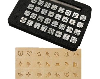 Könnte beinhalten: Ein Metallstempel-Set mit verschiedenen Formen und Symbolen, darunter Sterne, Schmetterlinge und geometrische Designs. Das Set enthält einen Griff und wird in einem schwarzen Schaumstoffetui aufbewahrt. Ein Muster der gestempelten Designs wird auf einer hellbraunen Oberfläche gezeigt.