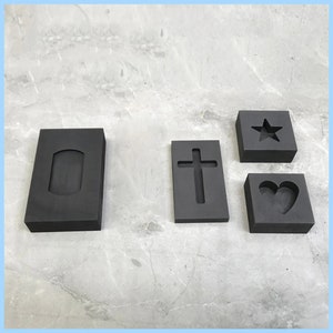 Puede incluir: Cuatro moldes de caucho negro para fundir metal. Los moldes son rectangulares y tienen diferentes formas cortadas: un rect&aacute;ngulo, una cruz, una estrella y un coraz&oacute;n.
