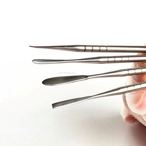 May include: Set of four stainless steel tools with different shaped tips. The tools have a ridged handle and are used for sculpting and shaping.