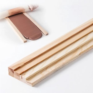 May include: Four wooden strips, two are longer than the other two, stacked on top of each other. The strips are light brown and have a smooth surface.