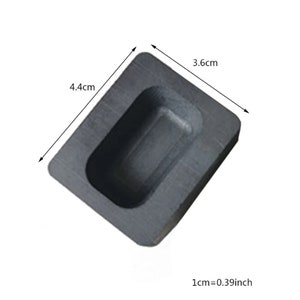 Puede incluir: Un molde de grafito negro para fundir barras de metal. El molde es rectangular con una cavidad rectangular en el centro. El molde mide 4,4 cm por 3,6 cm.