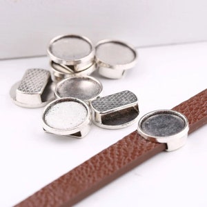 May include: Silver-toned metal round bezel settings for jewellery making. The bezels have a smooth, rounded edge and a flat back. They are designed to hold a cabochon or other flat-backed stone. The bezels are shown on a brown leather strap.