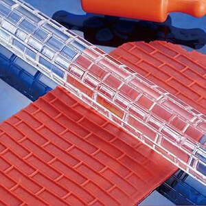 May include: A clear acrylic rolling pin with a brick pattern. The rolling pin is used to create an embossed brick pattern on fondant or dough.