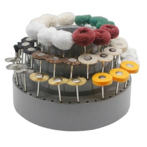 May include: A grey plastic rotary tool bit holder with a variety of different coloured and textured bits. The bits are arranged in a circular pattern around the holder.