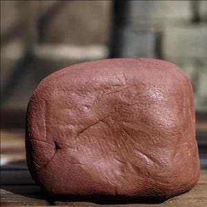 May include: A large, reddish-brown rock with a smooth, weathered surface. The rock has a rounded shape with a few visible cracks and indentations. The lighting suggests it is outdoors, possibly in a garden or natural setting.