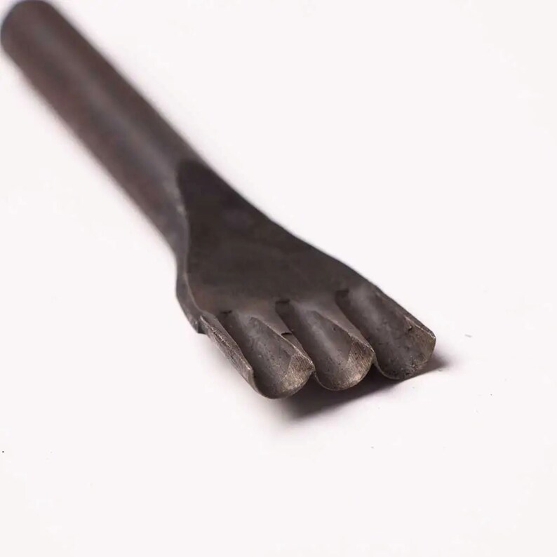Pu&ograve; includere: Un punzone per cuoio in metallo nero da vicino con quattro punte. Lo strumento viene utilizzato per creare fori nel cuoio per la cucitura.