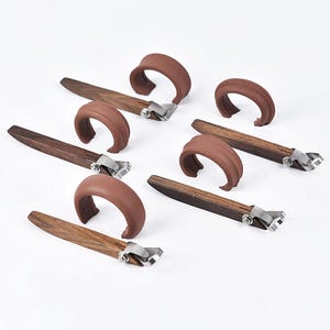 Op de afbeelding: Een verzameling bruine en zilveren wijnflesstoppers. Elke stopper heeft een donkerhouten handvat, een zilverkleurige metalen basis en een gebogen bruine rubberen afdichting. De stoppers zijn gerangschikt op een wit oppervlak.