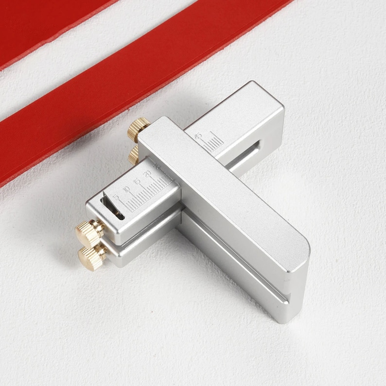 May include: A silver leather cutting tool with a ruler and two adjustable knobs. The tool is used to cut leather strips to a specific width.