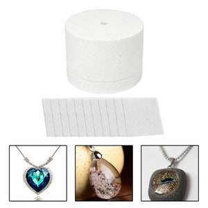 以下が含まれることがあります： 樹脂製のジュエリーを作るための白いフォームモールド。モールドは中央に穴のある円形です。画像には、完成した樹脂製のジュエリーの例が3つ示されています。青と緑の宝石がついたハート型のペンダント、透明な樹脂と茶色のインクルージョンがついた涙型のペンダント、透明な樹脂と金色のグリッターがついた正方形のペンダントです。