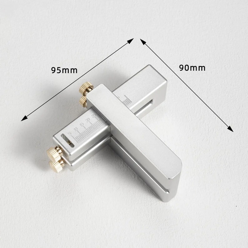 May include: A silver metal tool with a ruler and adjustable arms. The tool measures 95 mm by 90 mm.
