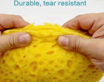May include: Close-up of a yellow sponge being stretched and pulled apart to show its durability and tear resistance. The sponge has a honeycomb-like texture.