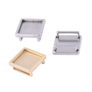 May include: Three metal square frames, two silver and one gold, with a raised edge around the perimeter. The frames are designed to hold a small picture or other decorative item.