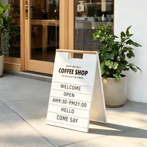 May include: A-frame sign for a coffee shop, with the text "COFFEE SHOP" in bold letters. The sign also includes the words "WELCOME", "OPEN", "HELLO", and "COME SAY". The sign is white with a wooden handle and is positioned on a sidewalk.