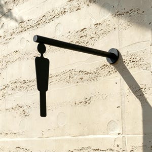 May include: A matte black metal wall-mounted sign featuring a minimalist silhouette of a person suspended from a horizontal rod. The sign is attached to the wall with a circular base, creating a clean, modern aesthetic with a distinct shadow.