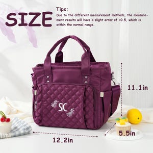 May include: A plum-colored tote bag with a quilted front pocket, embroidered with "SIC" and a leaf design. The bag has a top handle and a shoulder strap. Dimensions are 12.2 inches wide, 11.1 inches high, and 5.5 inches deep.