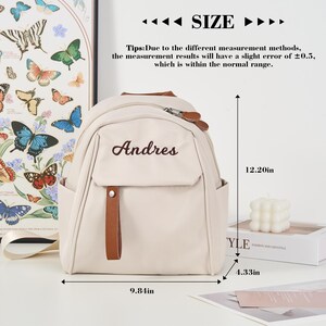 Puede incluir: Mochila beige con el nombre "Andres" bordado en la parte delantera. La bolsa tiene un bolsillo frontal con una correa marr&oacute;n y cierre de cremallera. Dimensiones: 30.99 cm de alto, 25 cm de ancho y 10.99 cm de profundidad. El texto "SIZE" est&aacute; arriba.