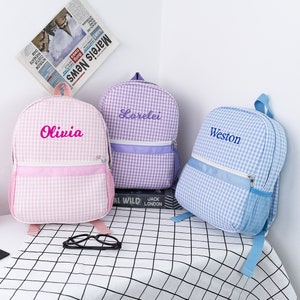 May include: Three personalized checkered backpacks in pink, purple, and blue with the names Olivia, Lorelei, and Weston embroidered on the front.