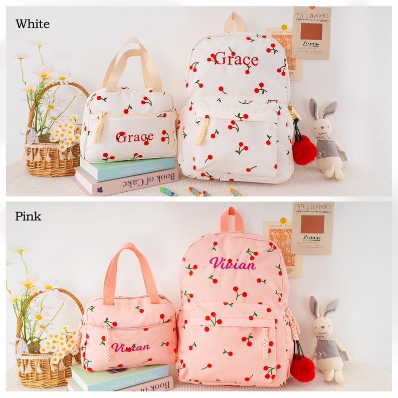 May include: White and pink backpacks and matching tote bags, both adorned with a cherry pattern. The white set has "Grace" embroidered, while the pink set features "Vivian". The bags are set against a light background.