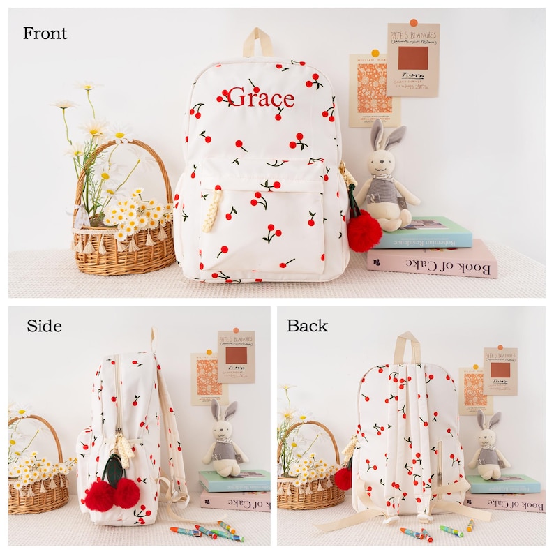 May include: White backpack with a cherry pattern and the name "Grace" in red script. The backpack has a front pocket, a top handle, and adjustable straps. The zipper pull has a red pom-pom.