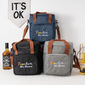 May include: Three insulated lunch bags with brown leather handles and adjustable straps. The bags are made of denim, black canvas, and gray canvas. Each bag has a personalized embroidered message that says "Teacher" with the teacher's name below.