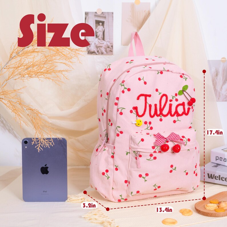 May include: Pink corduroy backpack with a cherry pattern and the name "Julia" embroidered in red. Features a bow and cherry accents. Dimensions: 17.4 inches high, 13.4 inches wide, and 3.2 inches deep.