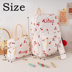 May include: A white backpack and matching tote bag, both adorned with red cherry patterns and the name "Grace" embroidered in red. The backpack measures 16.5 inches high, and the tote bag is 7.1 inches high.