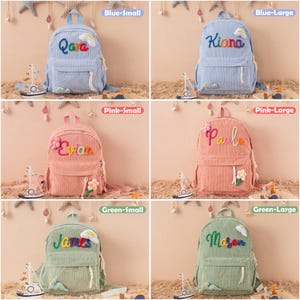 May include: A collection of corduroy backpacks in blue, pink, and green, each personalized with a name in colorful embroidery. The backpacks feature a front pocket, adjustable straps, and decorative embellishments. The image includes small toy sailboats.