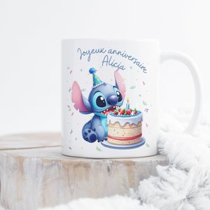 May include: White ceramic mug with a blue Stitch character wearing a party hat and holding a birthday cake with a lit candle. The mug says "Joyeux anniversaire Alicia".
