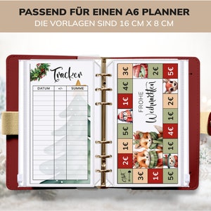 May include: A red A6 planner with a clear plastic cover. The planner has a tracker page with a Christmas tree design and a page with a Christmas themed design with the text "Frohe Weihnachten" (Merry Christmas) and various prices in Euros.