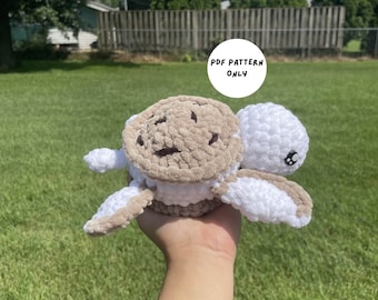 Puede incluir: Un juguete de amigurumi de tortuga tejido a crochet con una concha marrón y un cuerpo blanco. El juguete se está sosteniendo en una mano con un fondo de hierba verde. El texto "PDF PATTERN ONLY" es visible en la imagen.