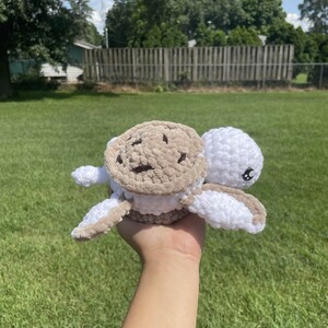 May include: A crocheted stuffed turtle toy with a brown and white shell and white body. The turtle has black eyes and a small, white mouth.