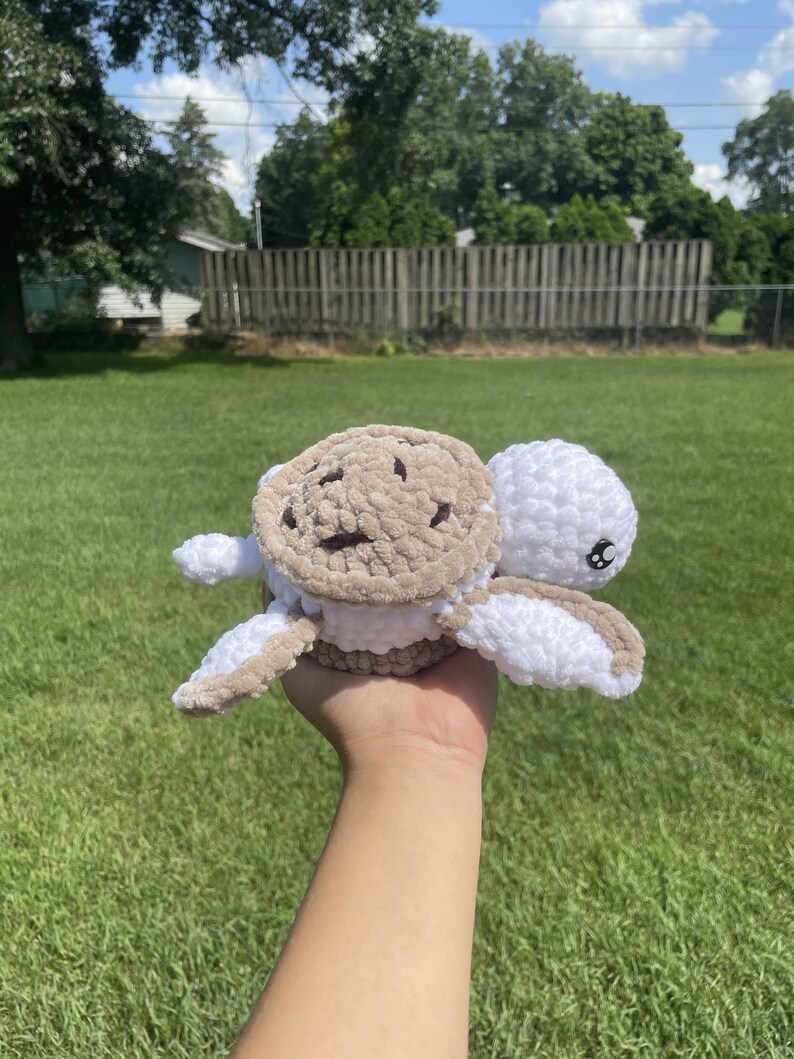 May include: A crocheted stuffed turtle toy with a brown and white shell and white body. The turtle has black eyes and a small, white mouth.