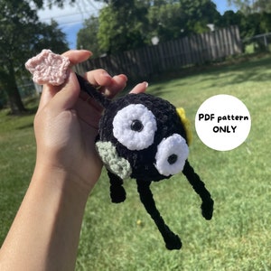 Może przedstawiać: Czarna pluszowa zabawka amigurumi wykonana na szydełku z białymi oczami i różowym ogonem w kształcie gwiazdy. Zabawka jest trzymana w dłoni. Na zdjęciu widoczny jest tekst "PDF pattern ONLY".