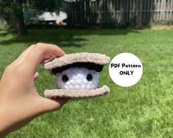 May include: A crocheted plush toy shaped like a clam with a white shell and brown edges. The clam has black eyes and a small black mouth. The toy is being held in a hand with a green grassy background. The text "PDF Pattern ONLY" is visible in a white circle.