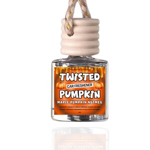 May include: A clear glass car air freshener with a wooden top and a woven string. The label reads "TWISTED PUMPKIN" with pumpkin illustrations and "MAPLE PUMPKIN NUTMEG" text. The scent includes pumpkin, maple, and spices.