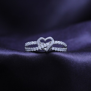 May include: A silver ring with a heart-shaped design set with small clear stones.