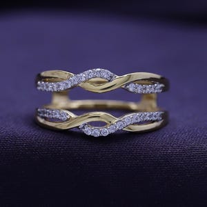 Op de afbeelding: Een gouden ring met een dubbelband ontwerp. De banden zijn met elkaar verweven en bezet met kleine, heldere stenen.